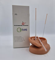 0,30x60mm TRIAS Akupunkturnadel mit Kupferwendelgriff und Führungsröhrchen auf einem Übungsohr positioniert und die Verpackung für hundert Nadeln im Hintergrund